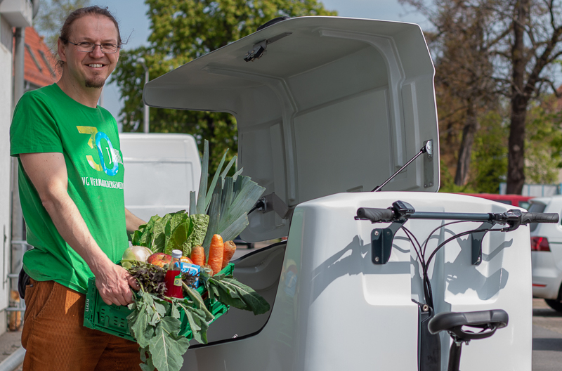 Mann hebt Kiste voller Lebensmittel auf Lastenrad